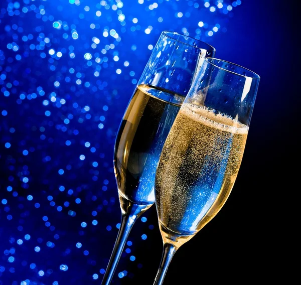 Champagne flutes with golden bubbles on dark blue light bokeh background