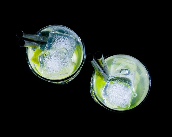 Top of view of glasses with cocktail and ice with lime slice on black background