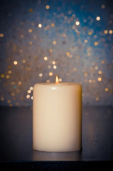 Candle with flame on wood table on blue bokeh background