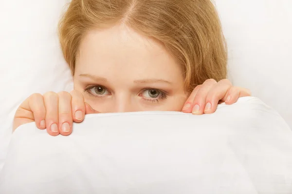 Cheerful girl looks out from under the blanket