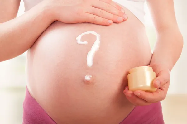 Belly of pregnant woman and question mark, painted cream