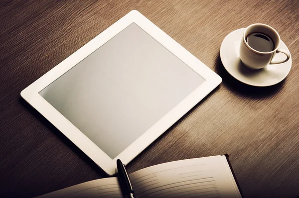 Tablet pc and a coffee and notebook with pen on the office desk