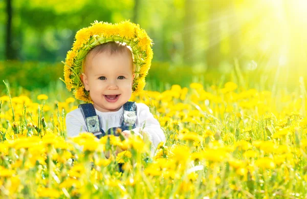 Happy baby girl in a wreath on meadow with yellow flowers on t