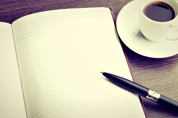 Open a blank white notebook, pen and coffee on the desk