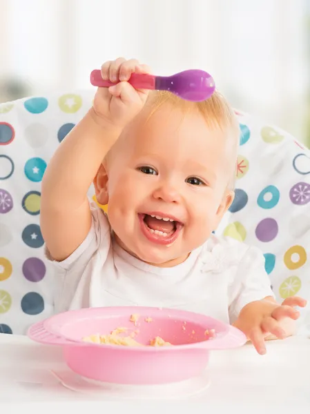 Happy baby child eats itself with a spoon