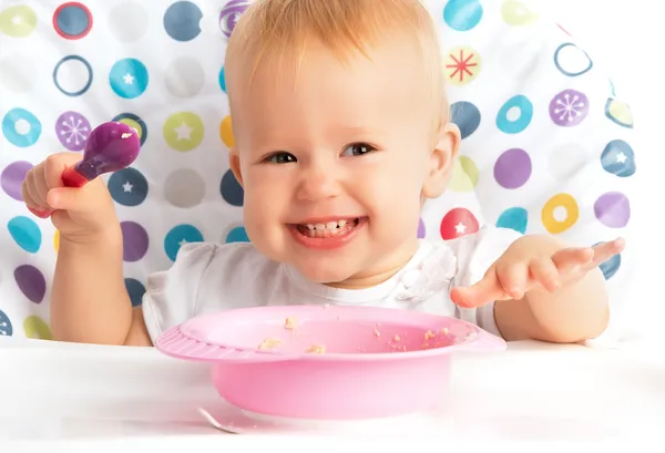 Happy baby child eats itself with a spoon