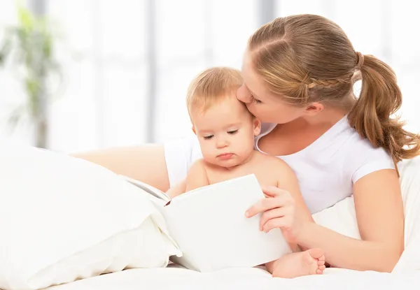 Mother reading book baby in bed before going to sleep