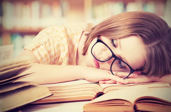 Tired student girl with glasses sleeping on books in library