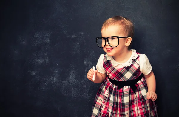 Funny baby girl  in glasses and chalk at a school board