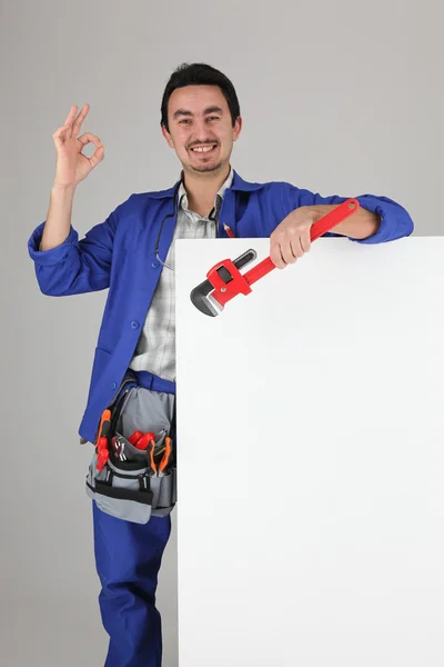 Tradesman giving the a-ok sign and standing behind a blank sign