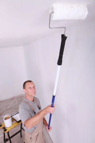 Decorator using roller to paint ceiling