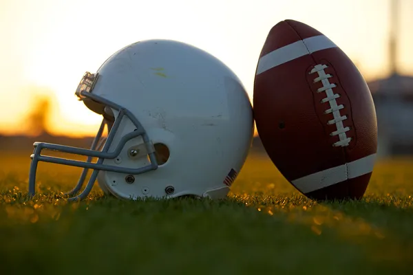 Football and Helmet on the Field at Sunset