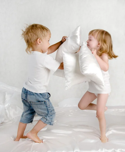 Happy laughing brother and sister having a pillow fight in bed at home