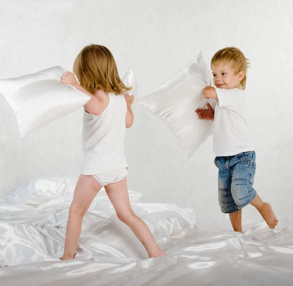 Happy laughing brother and sister having a pillow fight in bed at home