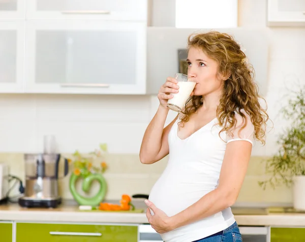 Pregnant woman drinking milk at kitchen