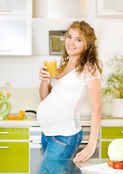Pregnant woman with glass of juice in the house kitchen