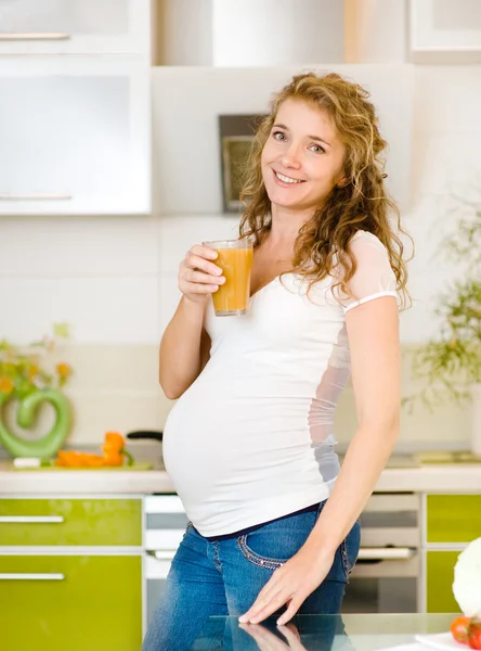 Pregnant woman with glass of juice in the house kitchen looking at camera