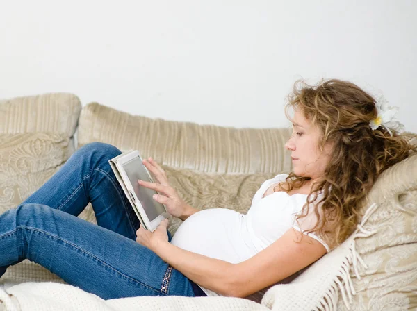 Pregnant woman lying down on sofa and reading ebook