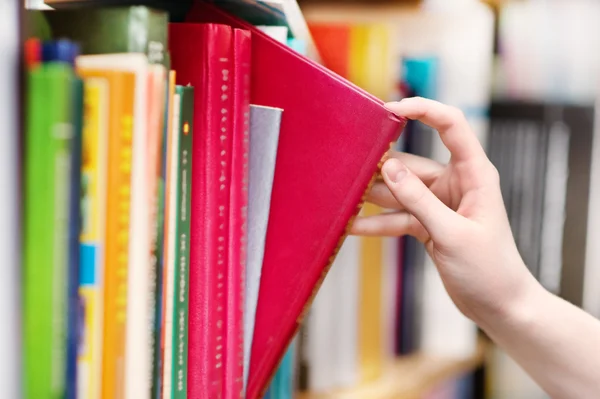 Closeup hand selecting book from a bookshelf