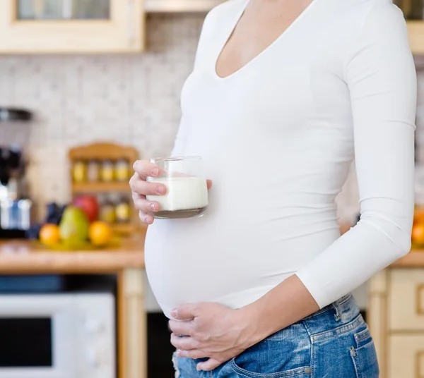 Pregnant woman with glass of milk in the house