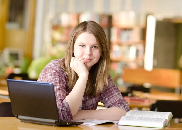 Female student with laptop and books working in a high school library