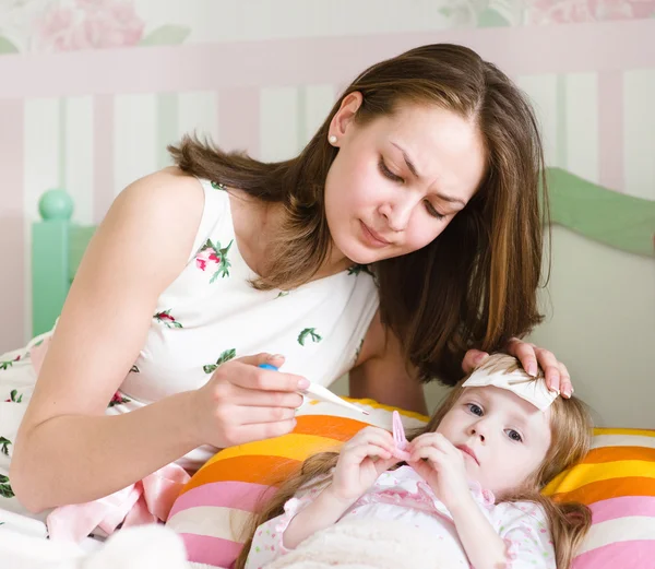 Sick kid with high fever laying in bed and mother taking temperature