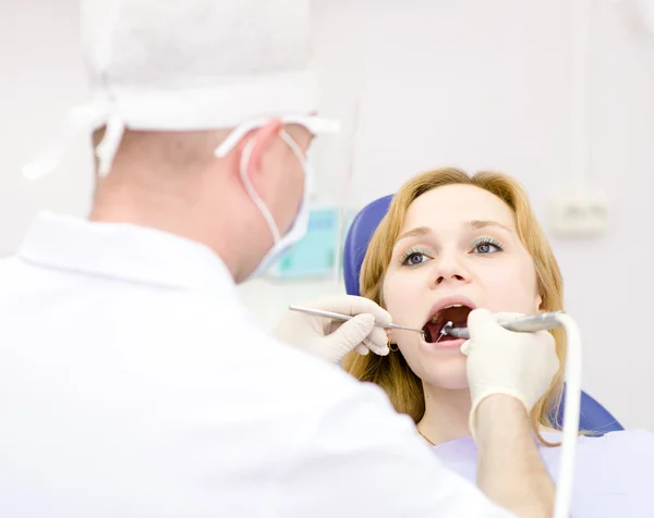 Young woman with open mouth during drilling treatment at the dentist