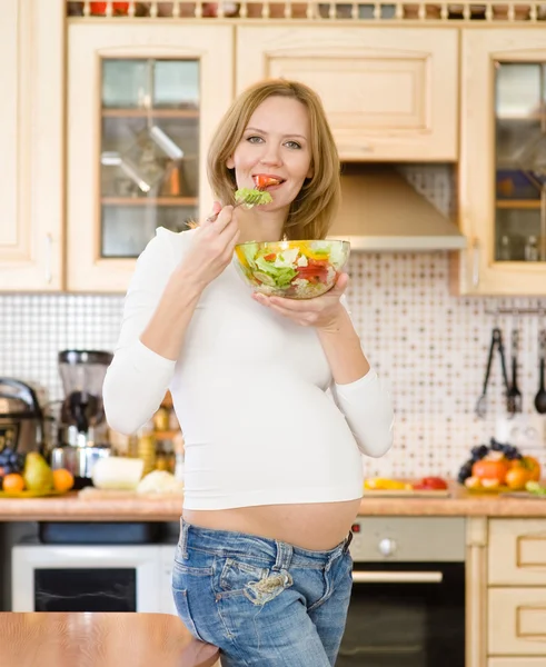 Pregnant woman in kitchen eating a salad