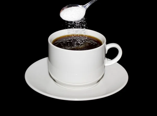 Sugar is poured from a spoon into a cup of coffee