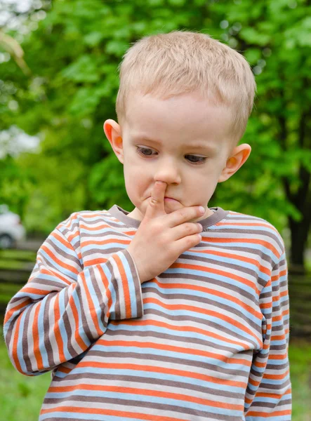 Little boy standing picking his nose