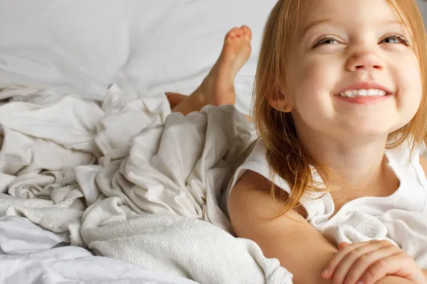 Smiling young girl in white covered bed