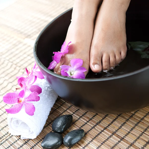 Feminine feet in foot spa bowl with orchids