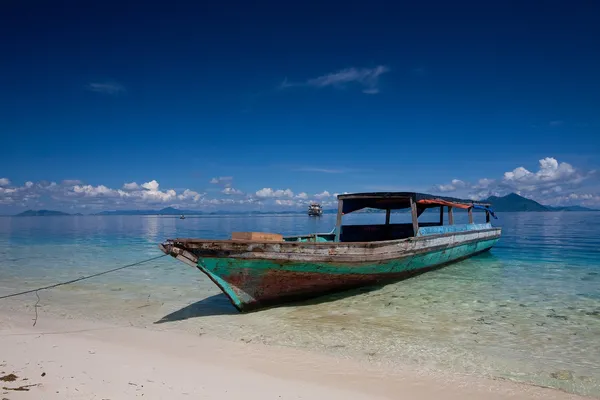 A lone wooden boat moored on crystal clear water of a tropical island.