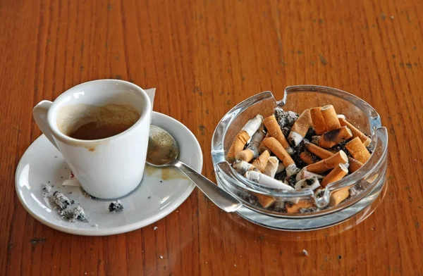 Ashtray chock full of cigarette butts and a cup of espresso