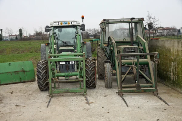 Two green tractors parked on a farm outdoors