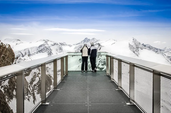 Two people looking at Alps mountains from viewpoint platform