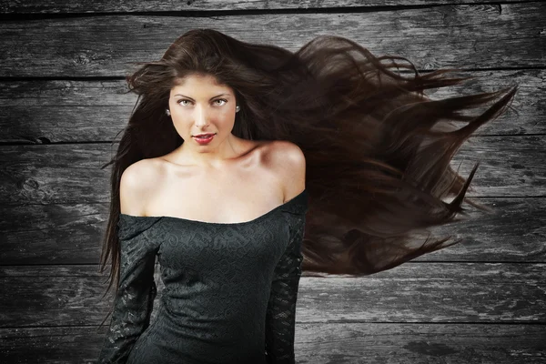 Young brunette woman with long flying hair, over wood background