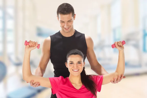 Woman with her personal fitness trainer exercising with weights in gym