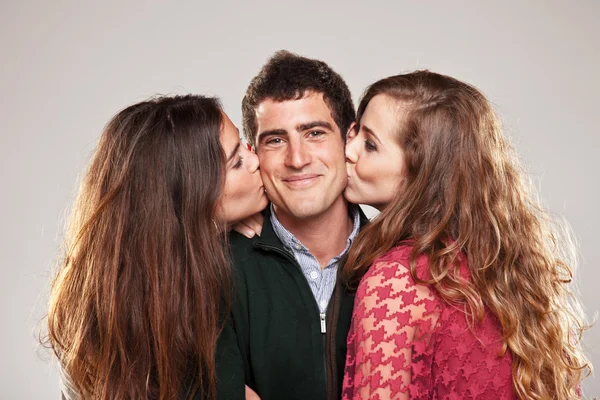 Two young women kissing handsome man standing between them