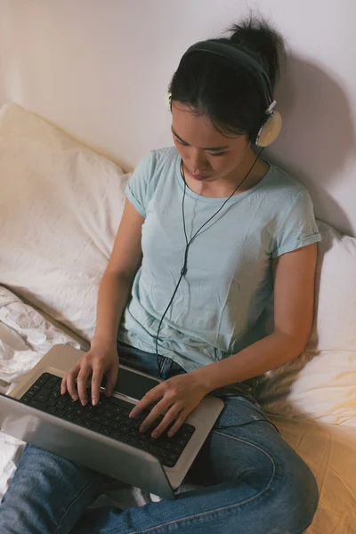 Casual young woman sitting on bed and using laptop at home.