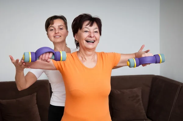 Coach assisting senior woman exercising with barbells