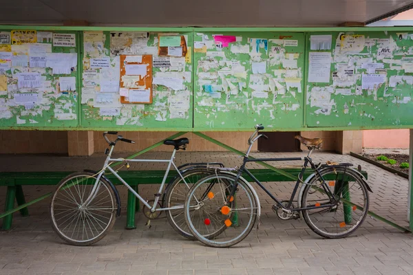 Two Old Bicycle Leaning Against A Bulletin Board On The Street