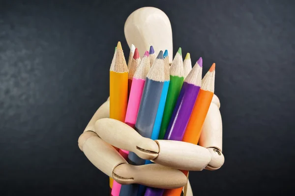 Wooden mannequin holds in hand a set of color pencils