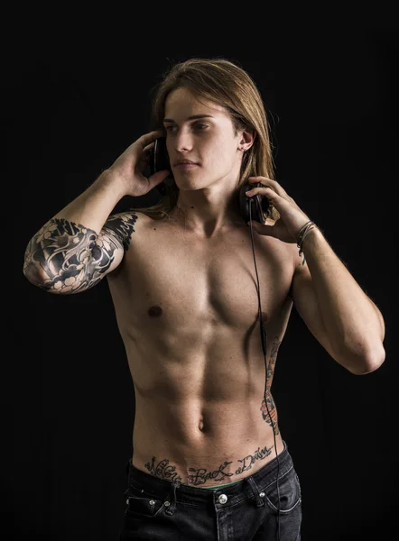 Man with tattoos shirtless listening to music