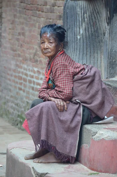 Poor elderly Nepalese woman sitting on the steps of the Palace to the Durbar square in Bhaptapure