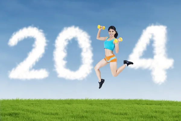 Fitness woman jumping with shaped clouds of 2014