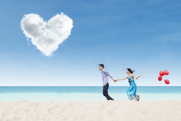Running couple at beach under heart cloud