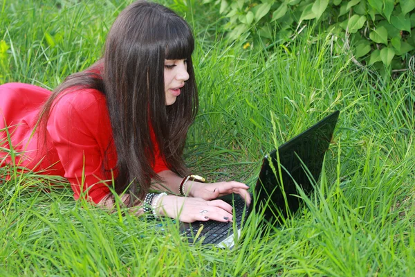 Girl with a laptop lying on green grass