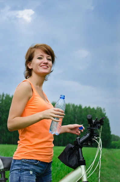 Young woman on bike drinking water from a bottle and smile