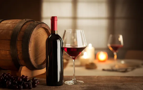 Cassa in legno con bottiglie di vino, botte, calici e uva su un ... Botte tavolo con vetro